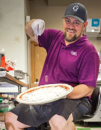 Scott Hutchinson making a pizza and smiling.